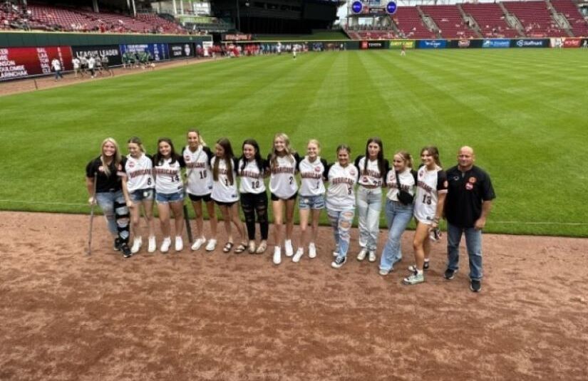 girls wearing baseball jerseys with coach on field